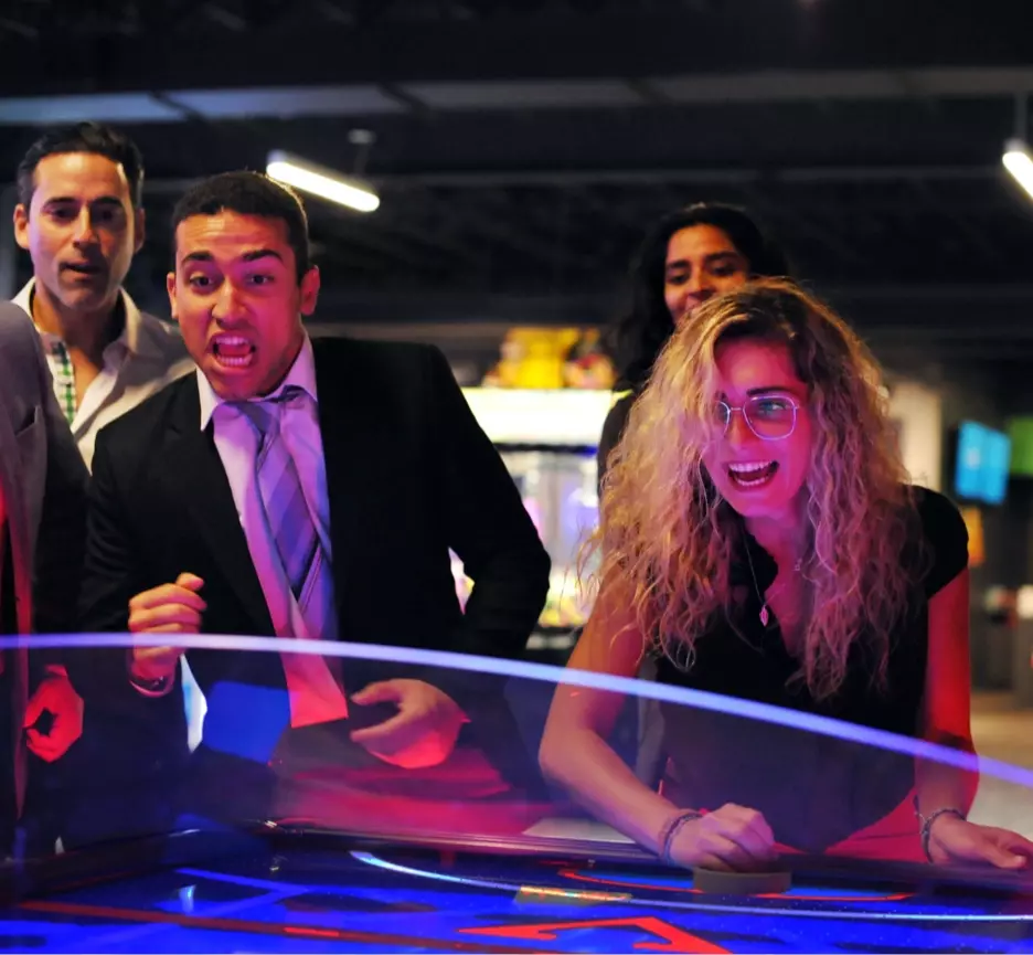 Group of adults watching their coworker play an intense game of air hockey in an arcade.
