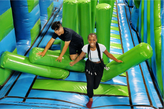 Two kids are energetically running through inflatable pillar barriers in an inflatapark. 