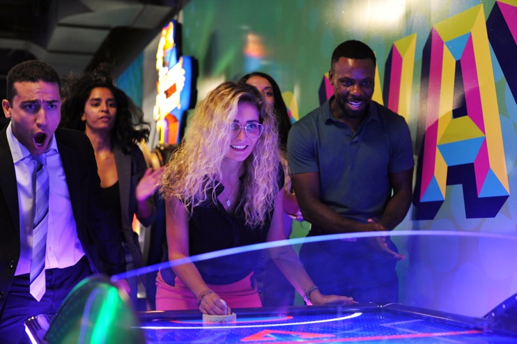 Group of adults watching their coworker play an intense game of air hockey in an arcade.