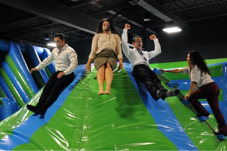 Group of adults bouncing and sliding down an inflatable hill in an inflatable arena. 